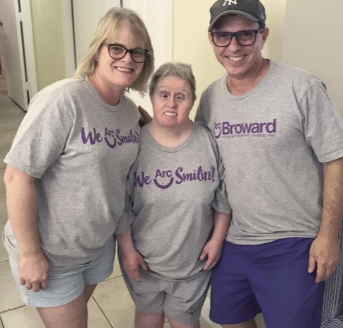 two adults in grey t-shirts posing with participant in grey t-shirt