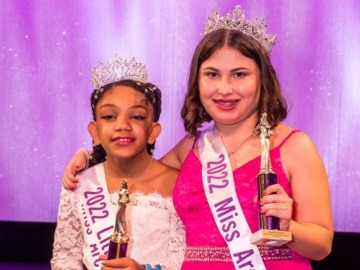 two young girls on stage holding pageant trophies