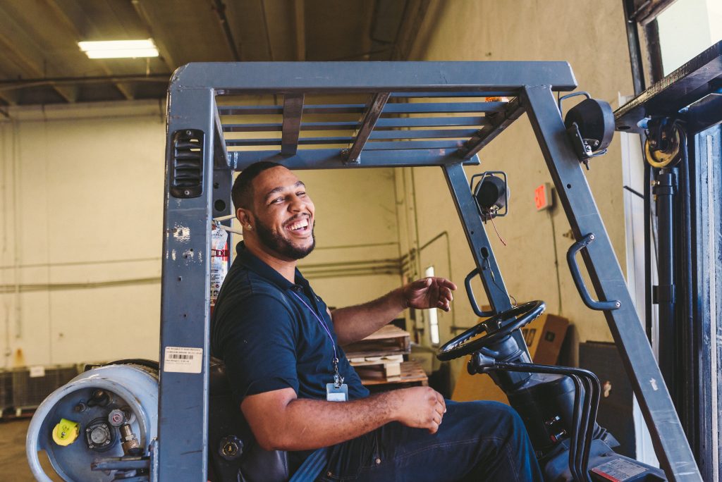 man in navy polo driving a forklift laughing