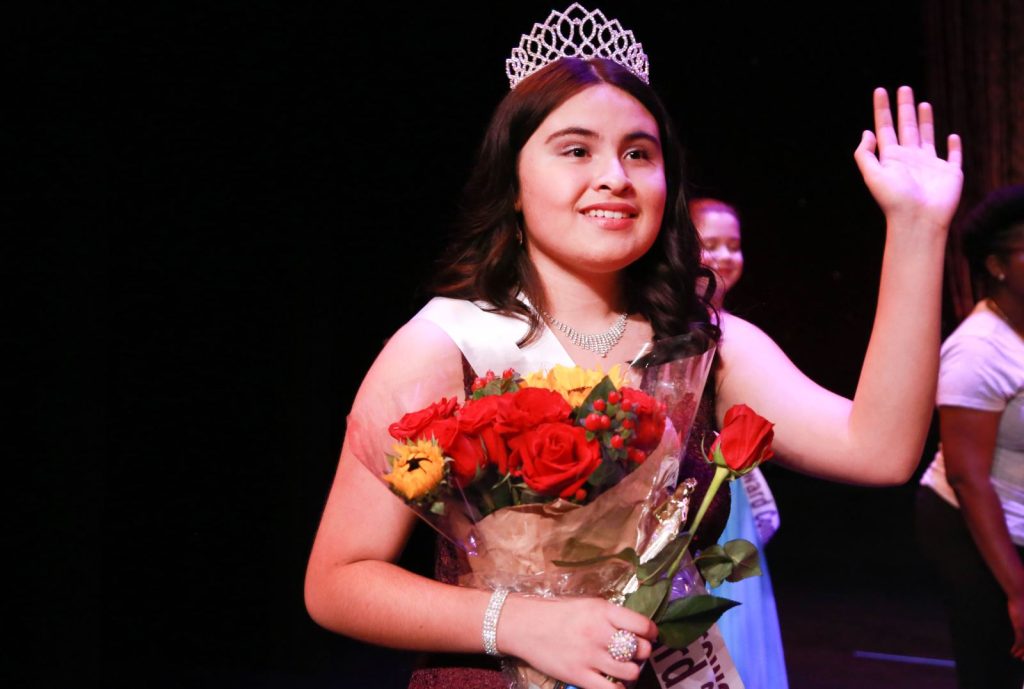 young girl with tiara accepting flowers on stage