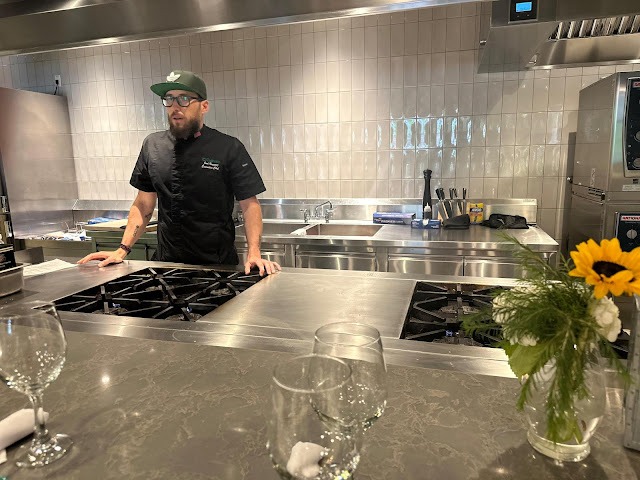 chef in black uniform and baseball cap stands alone in a commercial kitchen