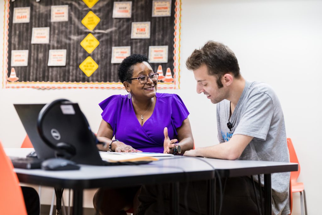 faculty member in purple dress has a discussion with adult student in grey shirt